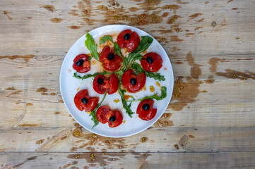 Tomatoes smashed with a fist, decorated with black olives and arugula arranged on a white plate on...