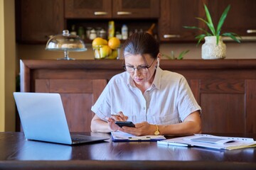 Home workplace, middle aged woman in headphones working using laptop