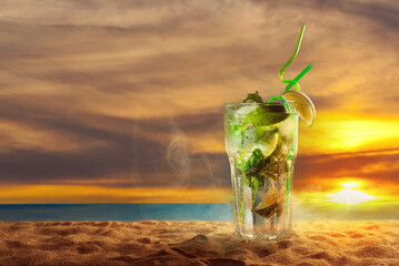 Green cocktail with a straw on the sand. Alcoholic mojito with ice, lime and mint on the beach....