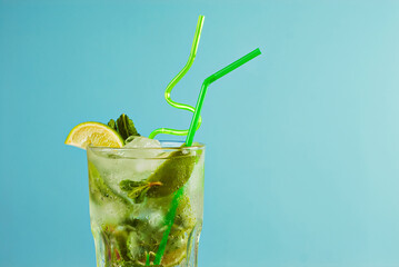 Green cocktail with straws on a blue background. Alcoholic mojito with ice, lime and mint close up.