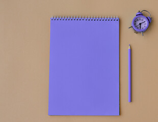 A notebook made of processed paper with a purple pen on a beige background with alarm clock. Home office