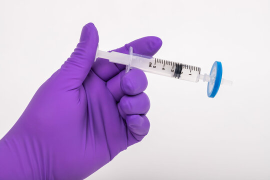 Scientist Holding A Needle Conducts An Experiment In The Laboratory. He Is Wearing Purple Gloves.