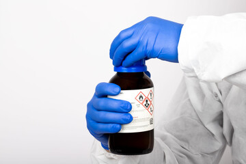 Scientist holding nitric acid in laboratory environment. It shows the way of use before the experiment. He has blue gloves on his hands