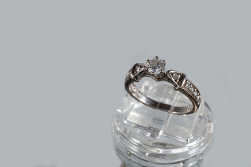 White gold ring with natural diamonds on a jewelry stand on a gray background
