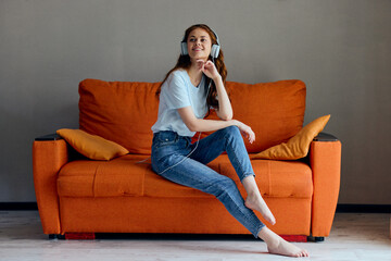 Obraz premium portrait of a woman on the orange sofa listening to music with headphones technologies