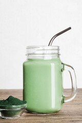 fresh green smoothie in glass bottle and spirulina powder with spoon on wooden background. useful habits, self care and healthy lifestyle. copy space