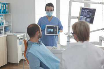 Medical nurse holding tablet computer explaining radiography diagnosis discussing teeth treatment...