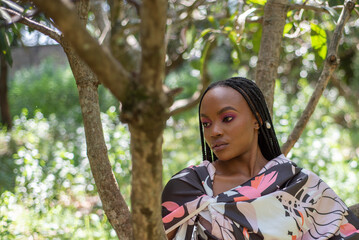 Portrait of Young African Woman standing under a tree in a mango orchard with long braids