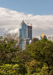 Obraz premium View of Modern high buildings among green trees space in nature against blue sky with clouds at afternoon. City growth concept, Selective focus.