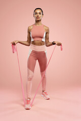 Sportswoman exercising with resistance band. Female with working out with elastic band on pink background