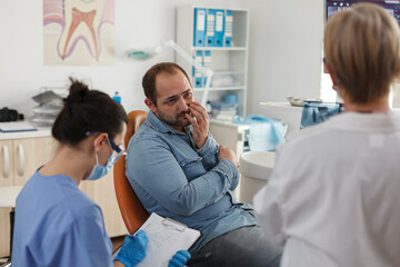 Obraz premium Specialist orthodontist team explaining oral hygiene to patient with toothache discussing medical expertise during stomatological consultation in dental office. Concept of medicine service
