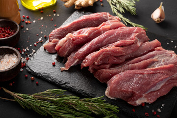 Pieces of fresh pork meat on a black table close up, raw meat with seasoning for cooking on a black board