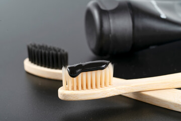 Bamboo toothbrush with charcoal paste on black stone table, closeup