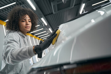 Focused young female detailer waxing client automobile