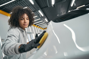 Serious service station worker waxing motor vehicle