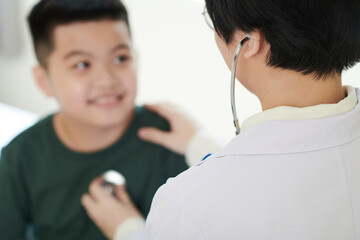 Rear view of female doctor examining the boy with stethoscope during medical exam