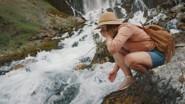 A woman traveler bent down to drink clean transparent water from a seething mountain river waterfall