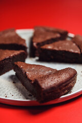 Fototapeta na wymiar Chocolate Flourless Cake on red background. Soft chocolate gateau or Brownie cake. Selective focus