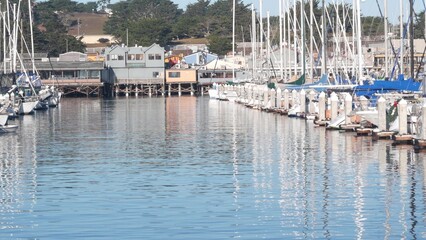Colorful wooden houses on piles, pylons or pillars, ocean bay or harbor, sea water. Old Fisherman's Wharf. Yachts, sail boats in Monterey Marina, California coast USA. Tourist beachfront promenade.
