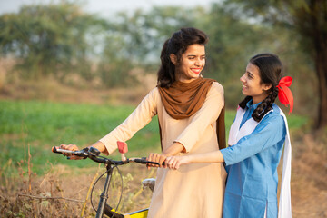 Portrait of happy young rural indian girls wearing school uniform standing with bicycle at village...