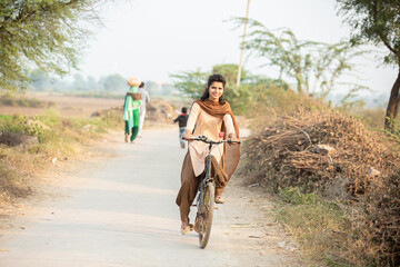 Young rural indian girl wearing school uniform ride on bicycle in village street.