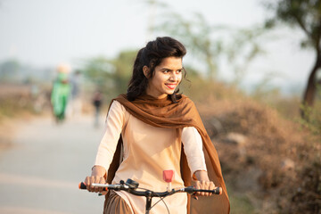Closeup of happy Young rural indian girl wearing school uniform ride on bicycle in village street.