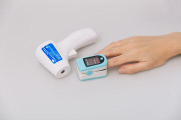 Pulse oximeter and thermometer gun on white background. Infrared isometric thermometer gun to check body temperature for virus symptoms. Measuring oxygen saturation, pulse rate and oxygen levels.