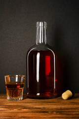 Glass and bottle of alcohol with a cork on a dark background.