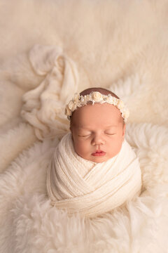 Sleeping newborn girl in the first days of life in a white cocoon with a white bandage on a white background. Studio macro photography, portrait of a newborn. The concept of female happiness.