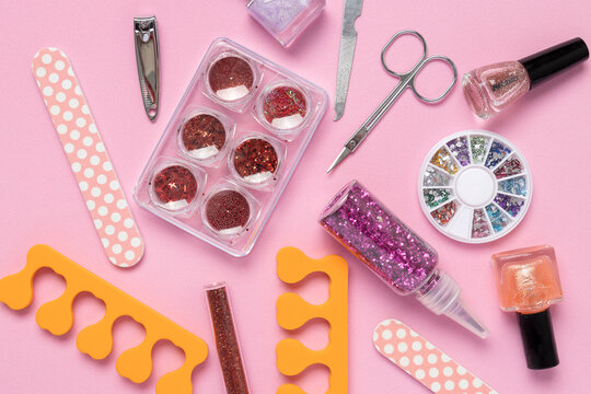Top view of shiny decorative gems,rhinestone for manicure,scissors,clippers for nail, bottles of nail polish, orange toe separators,nail files on the pink surface.Decor for nails as a background