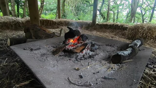 Wide angle bushcraft campfire burning with smoke in the daytime. Fire pit surrounded by straw hay bales.