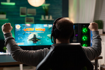 Player feeling happy after winning video games on computer. Man celebrating online win and playing games with headphones and monitor. Gamer using gaming technology and equipment.