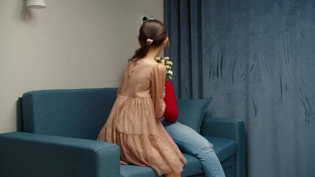 Lovely preteen girl congratulating her multiethnic mother with bunch of flowers at home. Touched female parent cuddling affectionate daughter expressing positive emotions indoors. Family relationships