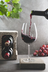 Bottle of red wine poured into the wine glass on concrete background. Vertical format. Beverage and...