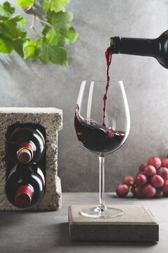 Bottle of red wine poured into the wine glass on concrete background. Vertical format. Beverage and wine concept.