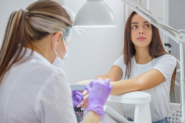 Fototapeta premium Closeup shot of woman in nail salon receiving manicure by beautician with nail file and machine. Woman getting nail manicure.