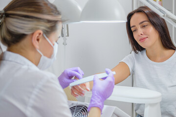 Closeup shot of woman in nail salon receiving manicure by beautician with nail file and machine. Woman getting nail manicure.