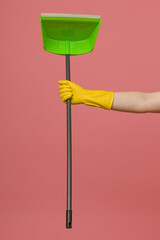 a hand in a yellow rubber glove holds a dustpan on a colored background