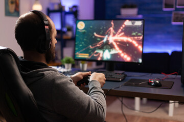 Person playing video games with controller on computer. Player using joystick and wearing headphones to play online game on monitor. Modern man using gaming equipment to have fun. © DC Studio
