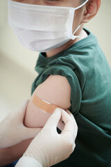 Close-up of doctor sticking the plaster on the arm of little boy in mask after an injection at...
