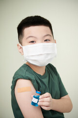 Portrait of child in mask holding the bottle with medicine and showing he getting vaccination from covid