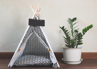 empty cloth gray pet  teepee tent with blank name tag beside plant pot on wooden floor and white wall. © Phuttharak