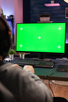 Close up of man using horizontal green screen on computer. Adult playing video games on chroma key with isolated mockup template and background on display. Gamer with technology and equipment.