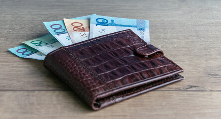 Belarusian money in a brown leather wallet on a wooden background. Banknotes of the Republic of Belarus. Belarusian currency. Selective focus, blurred background.