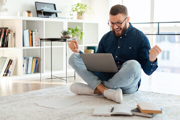 Joyful Male Using Laptop Shouting And Gesturing Yes Sitting Indoors