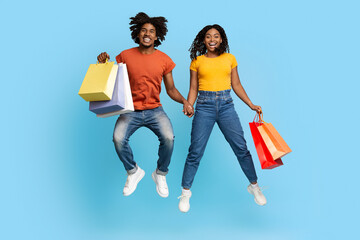 Happy african american lovers with shopping bags jumping up