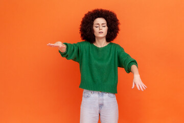 Blind woman with Afro hairstyle in green casual style sweater walking with outstretched hands,...