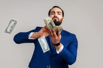 Fotobehang Bearded man scattering dollars with arrogant grimace, boasting wealthy life, concept of careless money spending, wearing official style suit. Indoor studio shot isolated on gray background. © khosrork