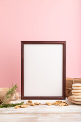 Brown wooden frame mockup with cup of coffee, almonds and macaroons on pink background. side view