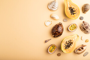 Ripe cut papaya, passion fruit, seashells, pebbles on orange pastel background. Top view, copy space.